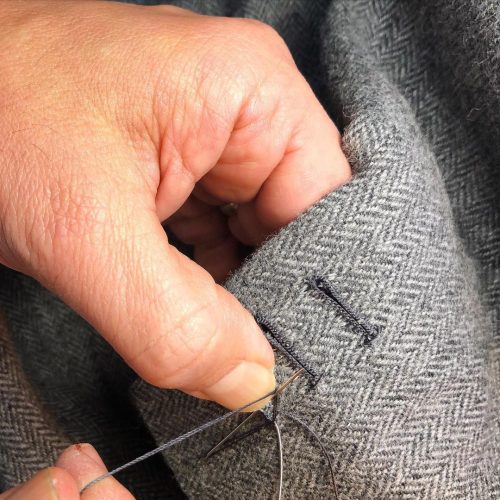 Closeup of a tailor stitching the button holes on a suit
