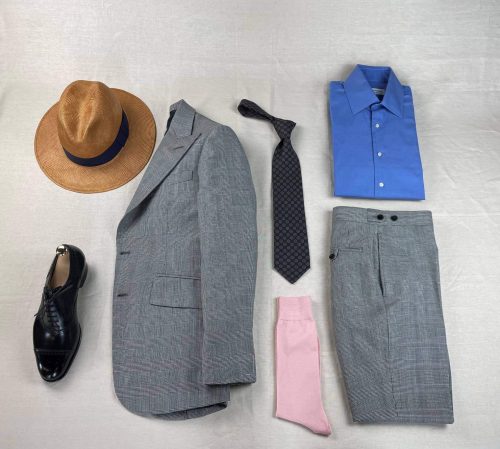 Grey suit laid out with a hat, shoes, tie, socks, and a blue collared shirt