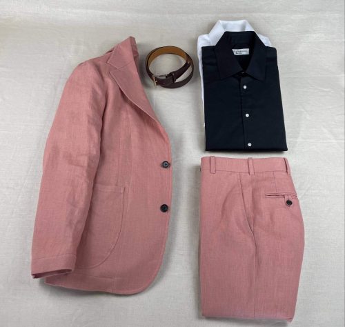 Salmon suit laid out with brown leather belt and a black collared shirt and a white collared shirt