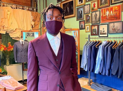 Model showing off a burgundy three piece suit along with matching face mask