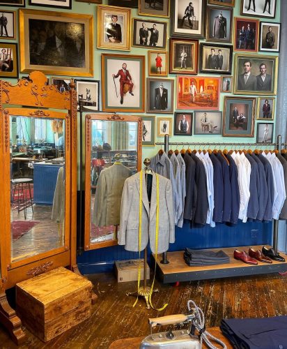 Wall of photos behind a mirror and a rack of suit jackets and dress shirts